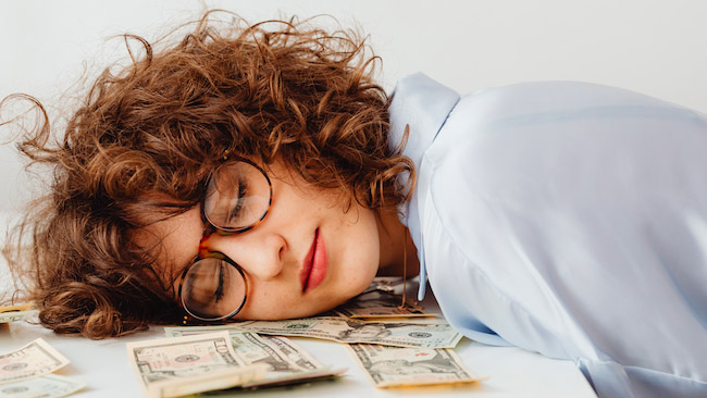 Une femme allongée sur des billets de banque, symbole de la confiance fragile dans le système bancaire et de la sécurité perçue de l’argent déposé en banque.